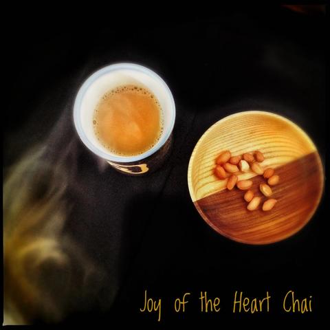 Joy of the Heart Chai, a masala chai with a lot of spices in small amounts. It sits in a cup next to a plate of red peanuts.