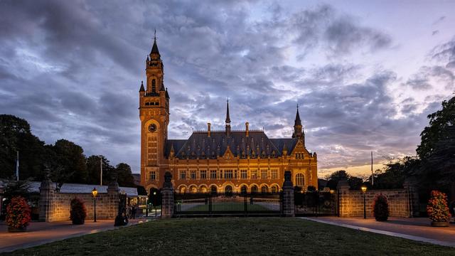 Large neo-classical building with one large tower and several small ones, in the foreground an ornamental gate across the width of the image.