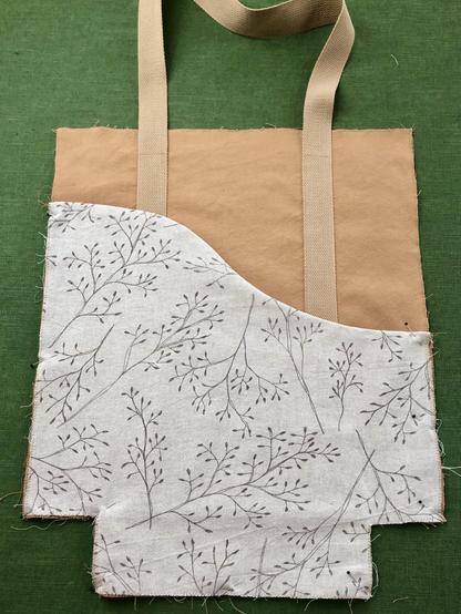Ein Taschenteil in geige und oocker mit aufgenähtem Furtband lieg auf grünem Leinenstoff