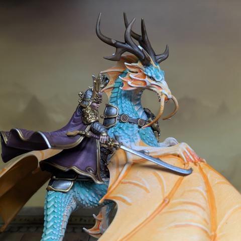A human in armour and purple robes rides a spirit creature not unlike a dragon, with bright orange wings and turquoise scales. It has long whiskers and tall horns.