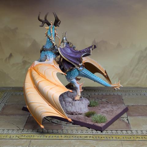A human in armour and purple robes rides a spirit creature not unlike a dragon, with bright orange wings and turquoise scales. It has long whiskers and tall horns.