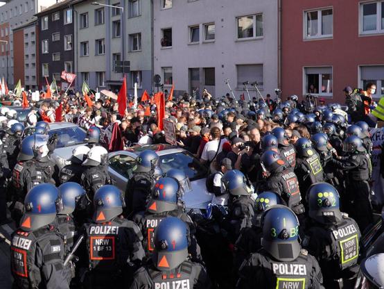 Demonstrationsgeschehen aus Köln von der Demonstration "Rheinmetall entwaffnen":.
Zahlreiche uniformierte und behelmte Polizistinnen und Polizisten in schwarzem Kampfanzug, die in einer Strasse, in der vierstöckige Wohnhäuser stehen, bedrängen. IN der Menge der demonstrierenden Menschen sind viele Flaggen zu sehen.