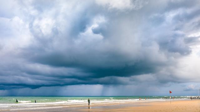 Paysage de plage de la côte atlantique avec l'horizon à l'arrière plan, à Lacanau. Un surfer sort de l'eau. Derrière lui se trouve d'énormes nuages menaçant et très contrastés, avec par endroits quelques gros voiles de pluie qui tombent en rideau des nuages