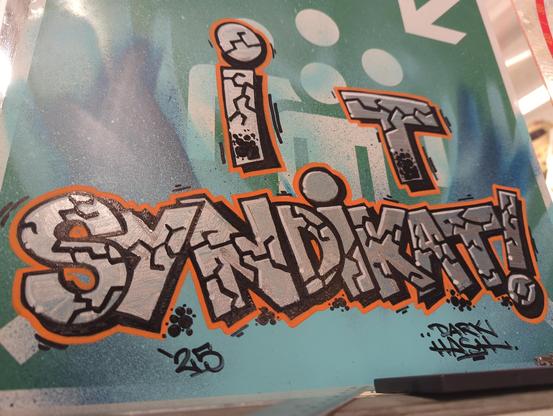 IT-Syndikat graffiti piece in silver-chrome, black and orange on a green street sign.