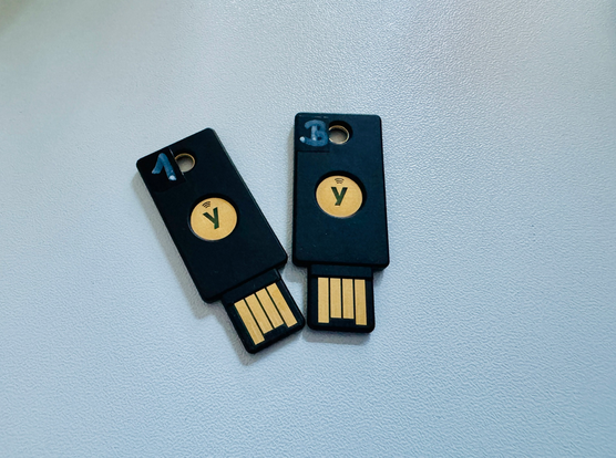 2 Yubikeys liegen auf einer weißen Platte. Auf dem linken Yubikey steht die Zahl 1, als Zeichen für den primären Stick, auf dem zweiten steht der Buchstabe B, als Zeichen für den Backup-Stick.