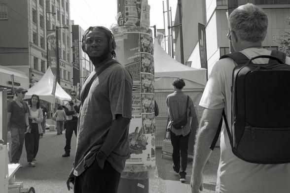 A man scans the street scene as pedestrians move through the frame.