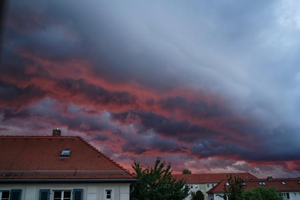 Wolken über Reihenhäusern, oben leicht hellgrau mit blau, unten grell rot bis schwarz