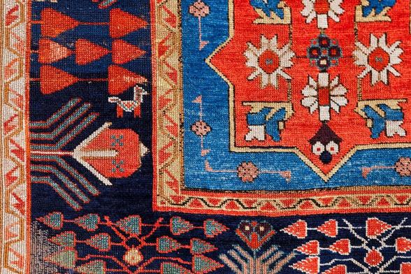 A patterned carpet largely woven in blue and red with a small stylized figure of a goat tucked among the other decorative elements.
