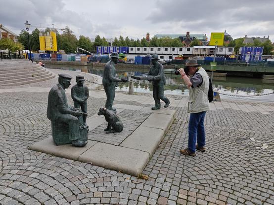 Die Bronze figuren hinter der Fischhalle: ein sitzender Mann und ein Junge füttern einen Hund mit Fisch, hinten bietet ein Mann Fisch auf einem Tablett an.