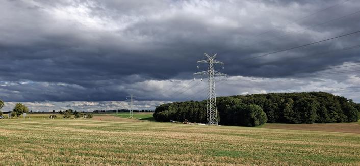 A view of a plain, in fact softly rolling hills. Transmission towers form a line to the horizon. A harvested field in the foreground, a minor forest midplain, a chain of hills forms the horizon.