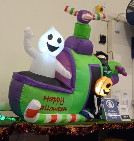 An inflatable helicopter. It is green and purple with an aeronautically infeasibly small rotor. There is a smiling ghost, of the white sheet variety,  piloting the helicopter and waving. There appears to be a pumpkin and witch attached to the back. On the side it says Happy Halloween (with no indication of the missing v).
Nearby signs say that it costs £69.99 and ask people not to touch it.