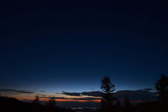 A wide angle view of the evening sky. The upper half of the frame is a dark blue that transitions to brighter tones that become yellow and orange just above the horizon. Some distant clouds are just above the horizon. The lights of the village of La Luz are on the basin floor.

See the next graphic for a finder chart of the brighter stars, constellations, and the planet Mars.