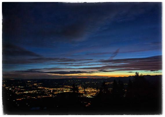 Light of a city in the night, captured from a mountain side. Dawn visible at the horizon.