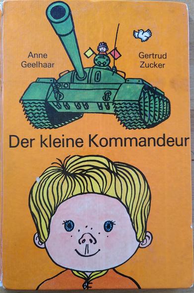 Titel eines Kinderbuches aus der DDR: "Der kleine Kommandeur". Ein kleiner Junge sitzt fröhlich im Turm eines Kampfpanzers, darüber flattert eine weiße Taube.