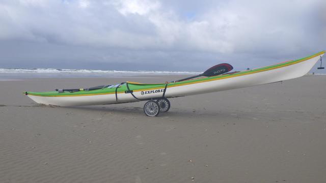 Seekajak auf einem Bootswagen auf einem weiten Sandstrand. Im Hintergrund sieht man Brandung.