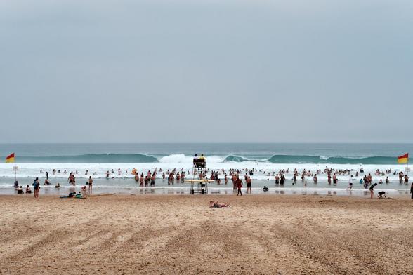 Foto eines mit Menschen vollen Strands mit hochen Wellen; Photo of a crowed beach with high waves