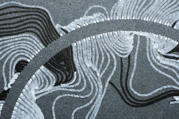 Macro closeup of the same flowing design with lines radiating away from a circle in organic forms. Printed with a pen plotter on dark cardboard in two rounds, first black india ink and then white ink on top, with me lifting the pen away manually to get areas without white. The closeup shows nicely how the white ink is thicker where the pen starts and ends.