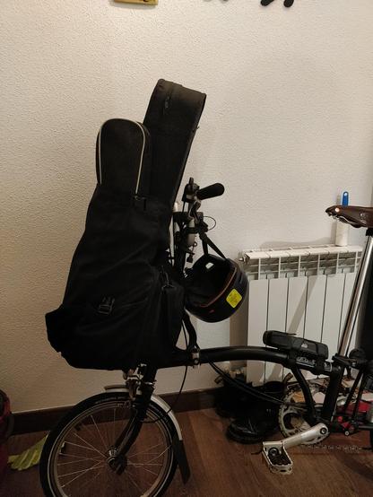 Una bicicleta plegable dentro de una casa. En su alforja delantera se puede ver como asoman dos fundas de instrumentos con forma que recuerda a un violín.