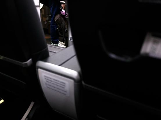 Out of focus pair of plane seats on the right side of a 737-800, looking through the gap between them to see feet boarding at door 1 of the plane.