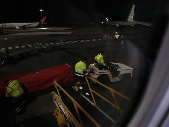 Ramp workers loading bags into a plane. A Qantas and Virgin Australia plane are visible behind them.