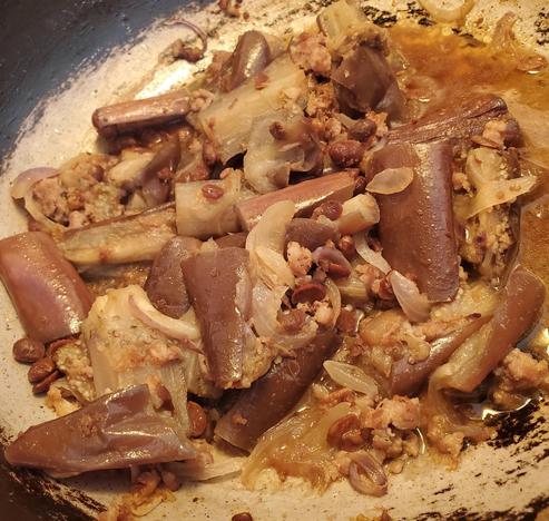 Close-up shot of cooked eggplant stewed with ground pork, preserved soybeans, and onions in a pan. Sections of the eggplant are purplish-brown.