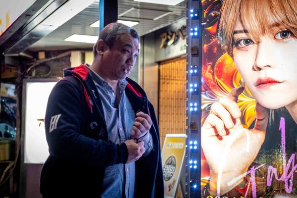 Home adult amb una cigarreta a la boca, passa davant d'un anunci lluminós de bar de hostos a Kabukicho.