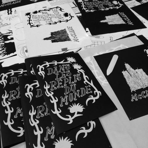 Table de travail avec des couvertures de zines sérigraphiées en noir et blanc en cours de pliage.