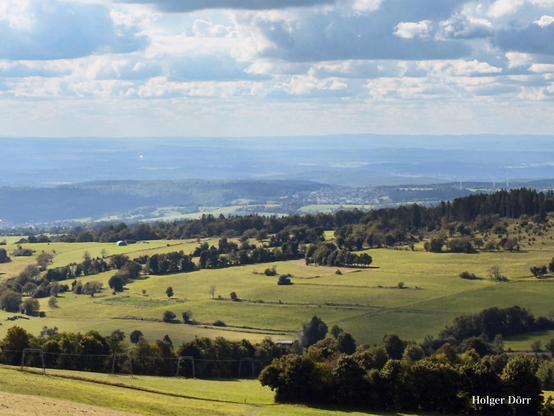 Weite Aussicht vom Hoherodskopf: sanfte Hügel und Wälder breiten sich bis zum Horizont aus, über ihnen ziehen helle Wolken, die dem Bild eine Atmosphäre von Freiheit und Fernweh verleihen.
