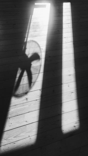 Two bright rectangles of light on a wooden floor, coming through windows, contrasting with the shadows, and a shadow cast by a fan