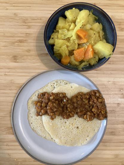 A flatbread with lentils on a plate, next to a bowl of turmeric coloured veg.