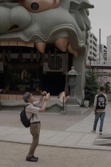 Man taking a photo with his phone while standing in front of a shrine in the shape of a lion's head.
