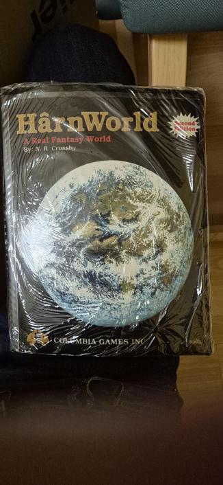 Foto vom Cover des HârnWorld Fantasy Atlas von Columbia Games Inc. Für das Hârnmaster Rollenspiel. Das Buch scheint ein Ringbinder zu sein, damit man es besser ohne Mittelfalz aufschlagen kann. Es ist noch in seiner original Tüte und unbenutzt.