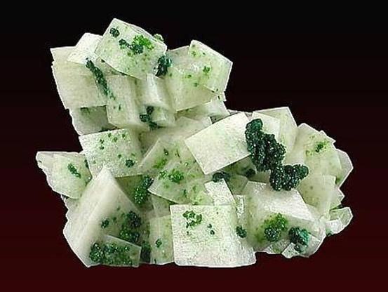 Photograph of a cluster of milky white rhombohededral calcite with bright green crystals of mottramite. Location: Tsumeb mine, Namibia. Image credit: Dan Weinrich, Geoffrey Krasnov