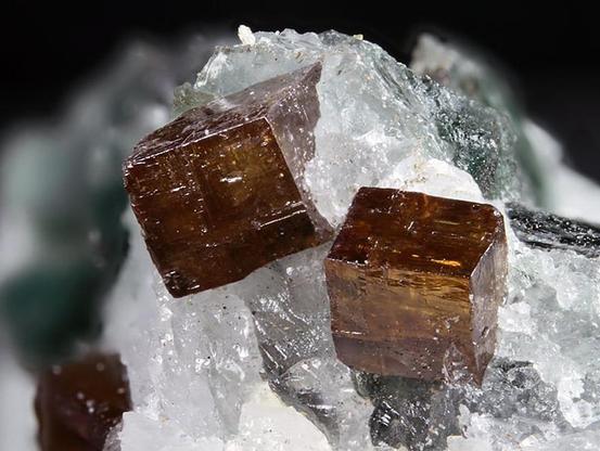 Image of two brown, pseudo-cubic perovskite crystals. Location: Rocca Sella dikes, Italy. Image credit: Matteo Chinelatto