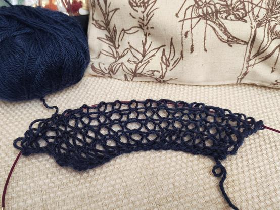 A small swatch of dark blue, very loose knitting lying on a beige couch cushion