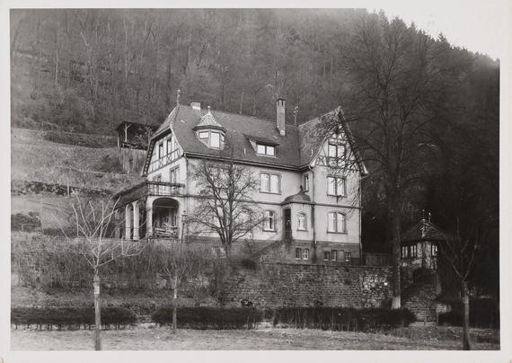 Schwarz-weiß Aufnahme des ehemaligen Wertheimer Volksbads. Zu sehen ist ein großes Haus im Herbst oder Winter. Die lange Hecke davor ist unbelaubt, auch die beiden Bäume im Vordergrund und auf dem steilen Berg, der hinter dem Haus hochgeht, sind ohne Blätter.