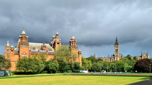 Ornate Victorian buildings lit by sunshine against distant storm clouds.