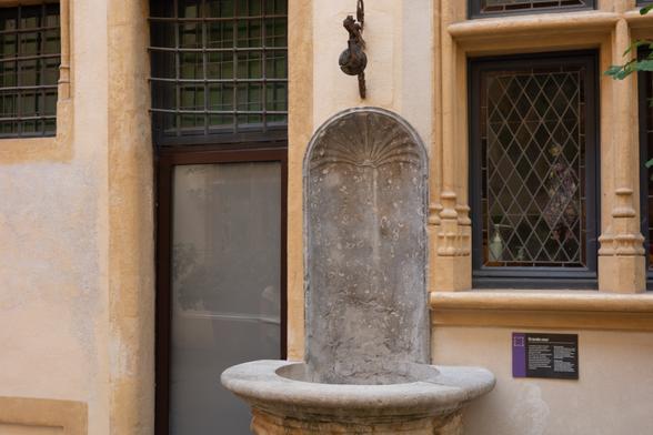 Tall, concave backsplash that has a scallop design on the arched top. Lower part is a well, though no water in it anymore. Above the stone is a wooden pulley.