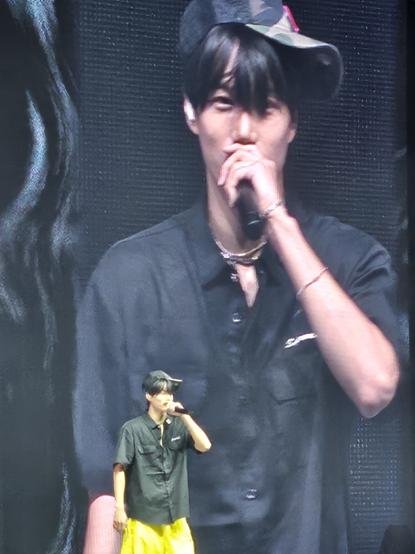 Kpop group EXO's Kai on stage during soundcheck with a giant video screen behind him. He's wearing a camouflage baseball cap with the Chicago 'C' sideways on his head while speaking into the microphone.