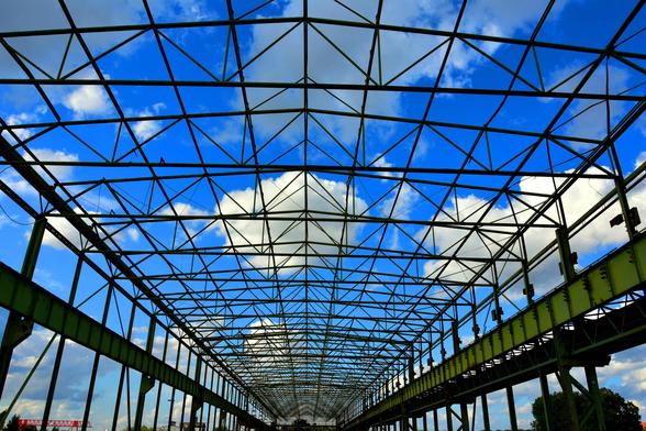 Steel truss roof structure of an industrial building with green beams and a blue sky with clouds in the background.

Dachkonstruktion eines Industriegebaeudes mit einem Gitter aus gruenen Stahltraegern und einem blauen Himmel mit Wolken im Hintergrund.