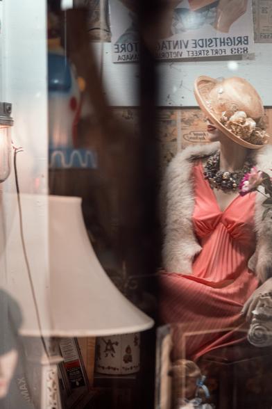 A mannequin patiently waits in the pale glow of a shop window.
