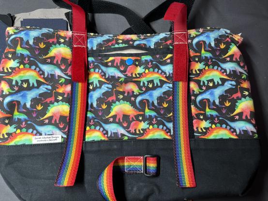 A photograph of the bag back, showing the three remaining rainbow straps (two to mount to the handlebars, one at the bottom to wrap around the fork shaft.  The bag is black with bright rainbow dinosaurs all over.