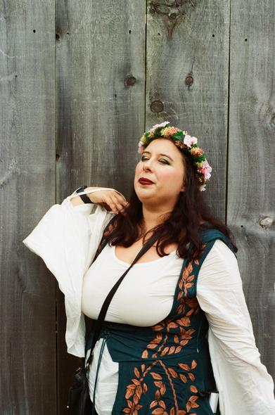 A woman poses proudly in her Renaissance costume in front of a fence.