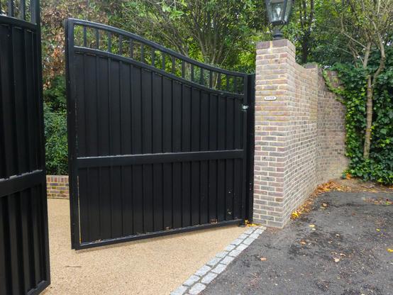 Black metal gates are ajar, showing a little of a driveway and garden behind. On a wall beside the gate a small sign reads "Enter"
