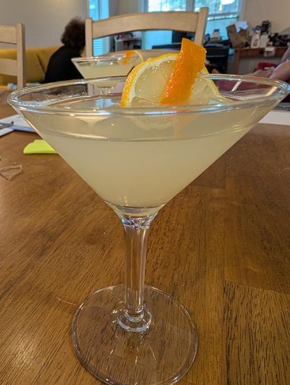 A martini glass with a drink garnished with a lemon slice and orange rind