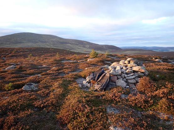 Photo of evening light on cairn at top of Crannach Hill. Our rucksacks are leaning against it. Big Morven in the distance.