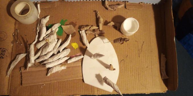 Paper-mache pointy teeth on a cardboard tray with a cap of water/glue mixture. 7 out of the 27 teeth are still the paper bag material base shaped in a rough tooth shape. A roll of medical tape and safety pins on the tray. 4 "teeth" are mounted on pins. 2 finished and 2 unfinished
