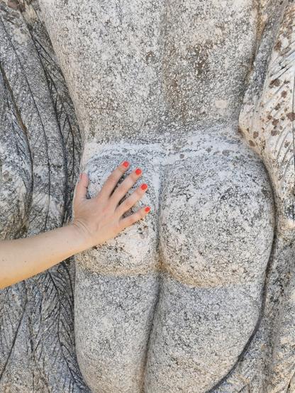 A hand gently touching a stone sculpture's detailed figure.