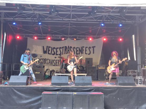 Band auf der Bühne. mitte und rechts sind 2 Frauen, links ein Mann. im Hintergrund ein Banner "Weisestraßenfest"