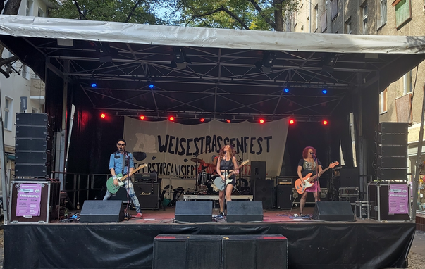Band auf der Bühne. mitte und rechts sind 2 Frauen, links ein Mann. im Hintergrund ein Banner "Weisestraßenfest"